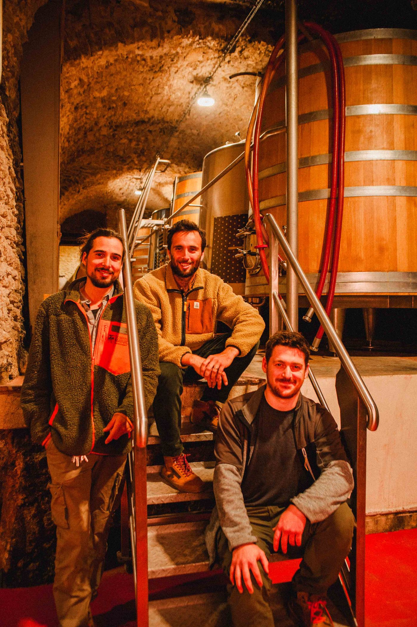 Arthur, Hugo et Jean assis sur l’escalier du chai voûté, devant un foudre en chêne